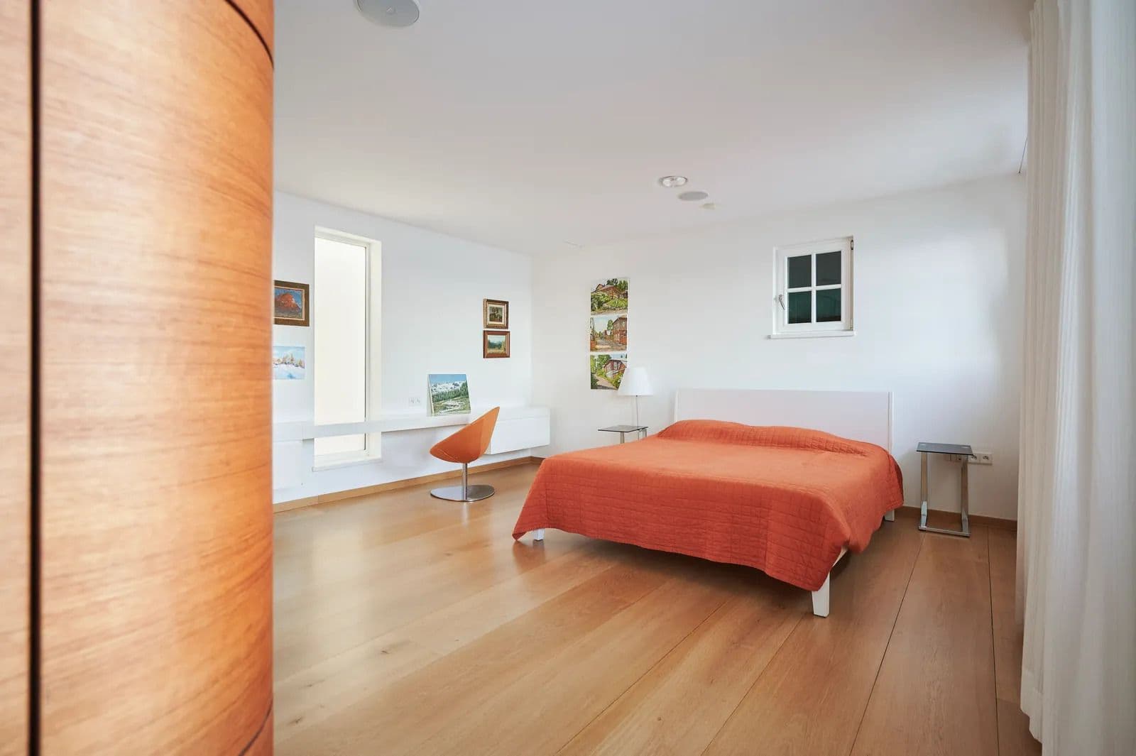 Guest bedroom with oak flooring, a rust coloured bedspread and a small seating area by the window.