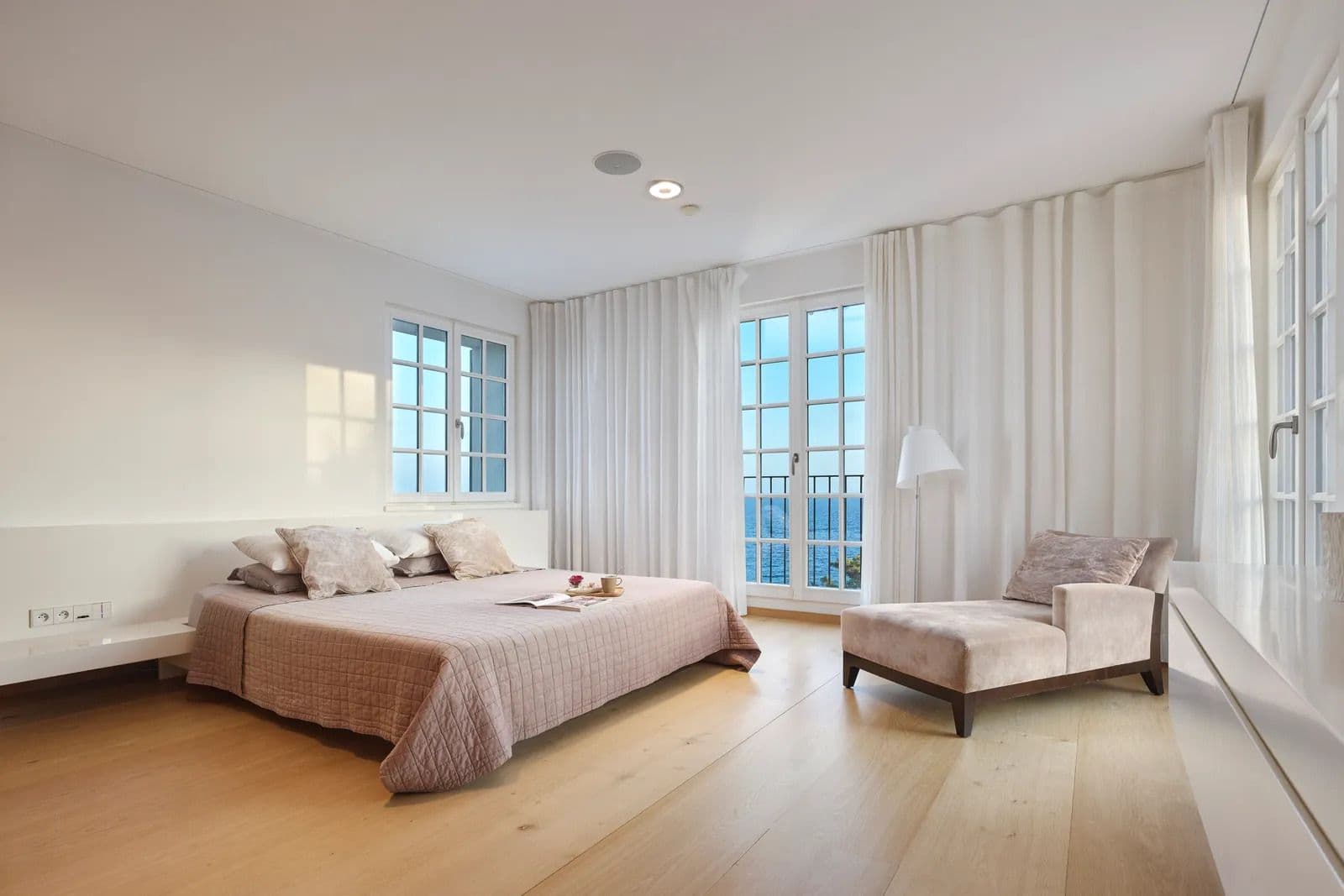 Bright bedroom with a low platform bed and floor to ceiling windows opening onto a sea view terrace.