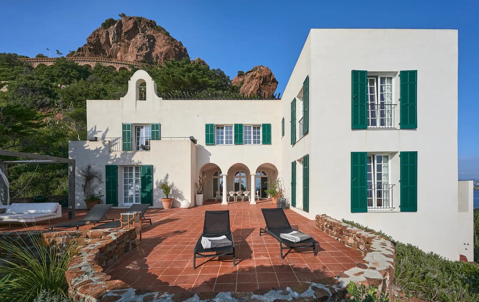 Courtyard view of the whitewashed villa with green shutters, terracotta paving and sun loungers.