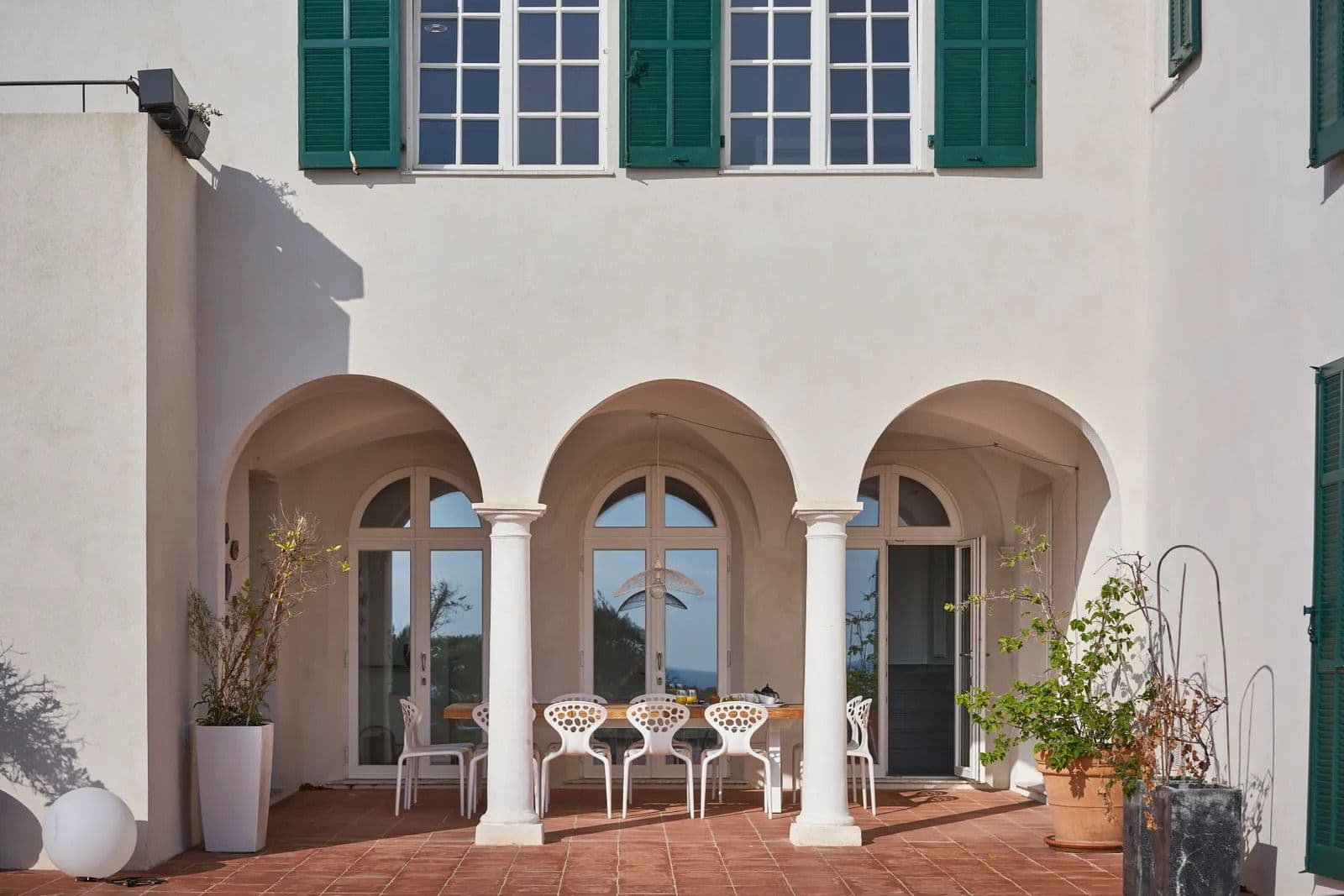 Arched loggia terrace with stone columns and an outdoor dining table set for guests.