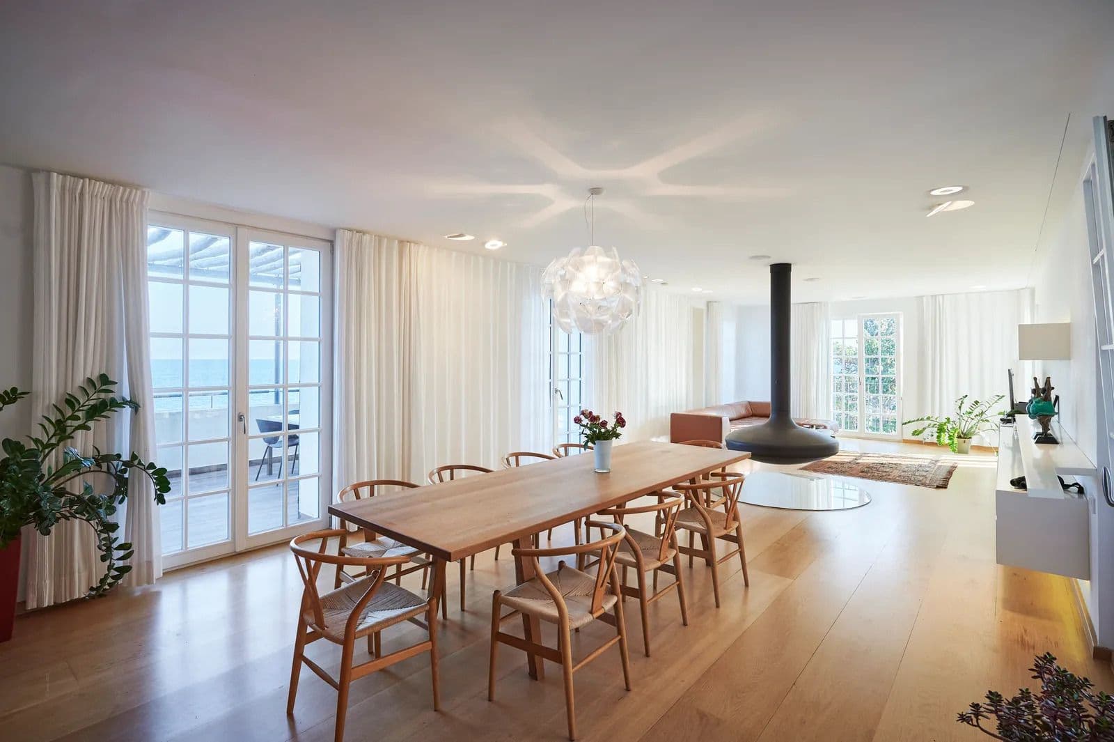 Open plan living and dining area with a long wooden table, wishbone chairs and full height glazing to the terrace.