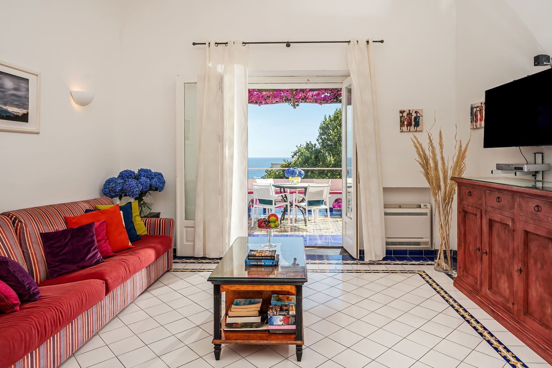 Living room with red sofa and doors opening to the pool terrace at Graceful Sea