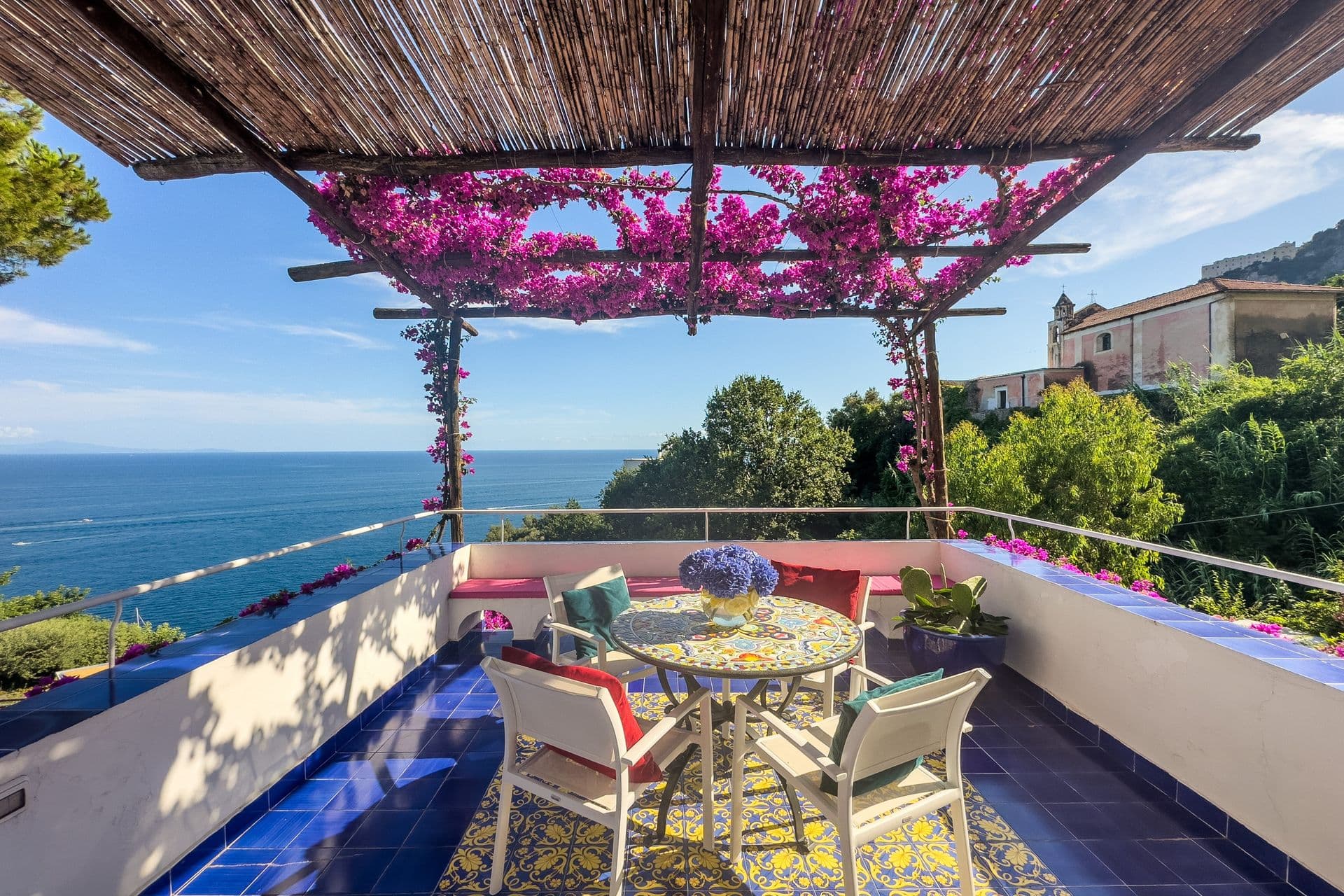Bougainvillea-covered pergola terrace with dining table and sea view at Graceful Sea