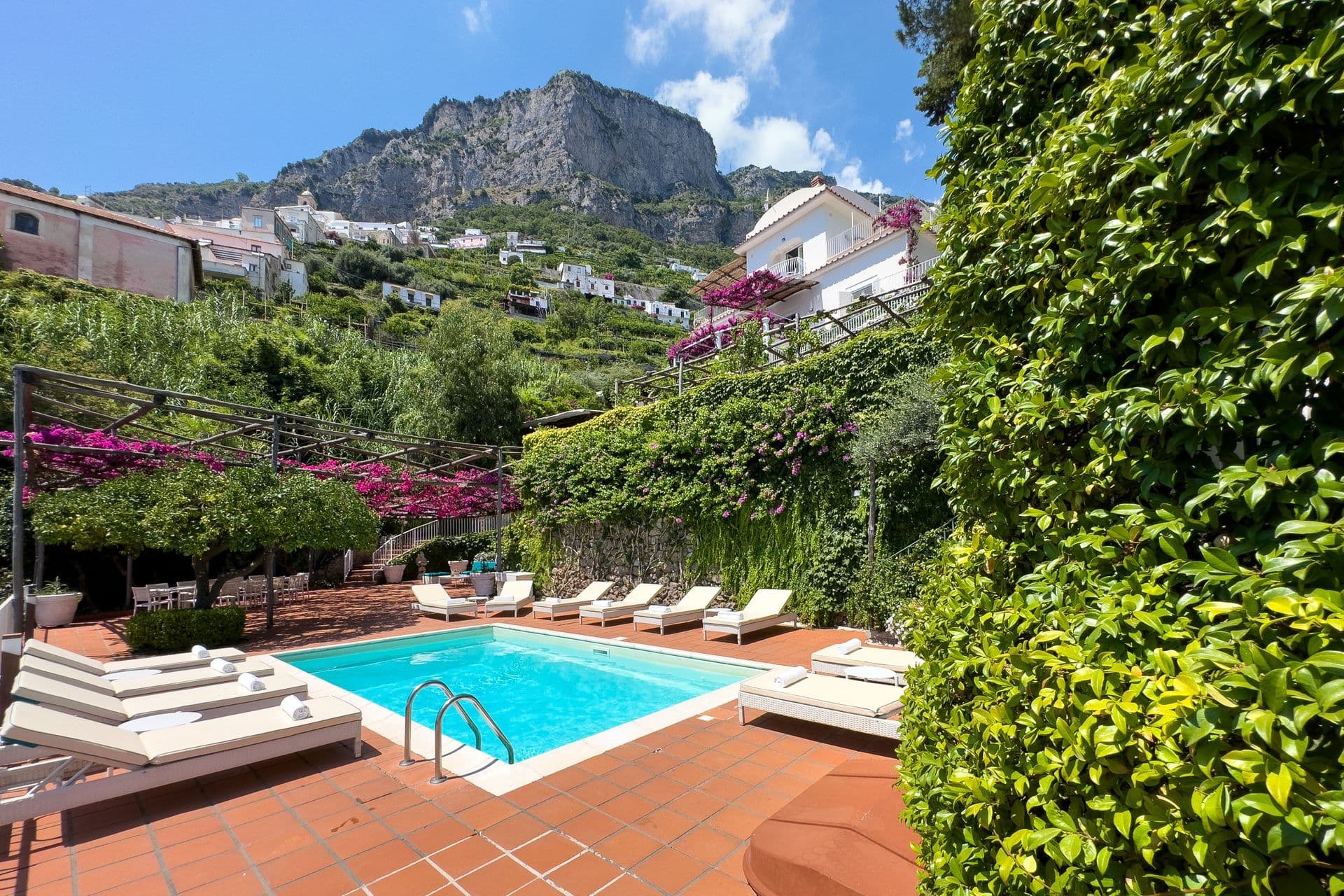 Pool terrace with sun loungers framed by the hillside village and cliffs at Graceful Sea