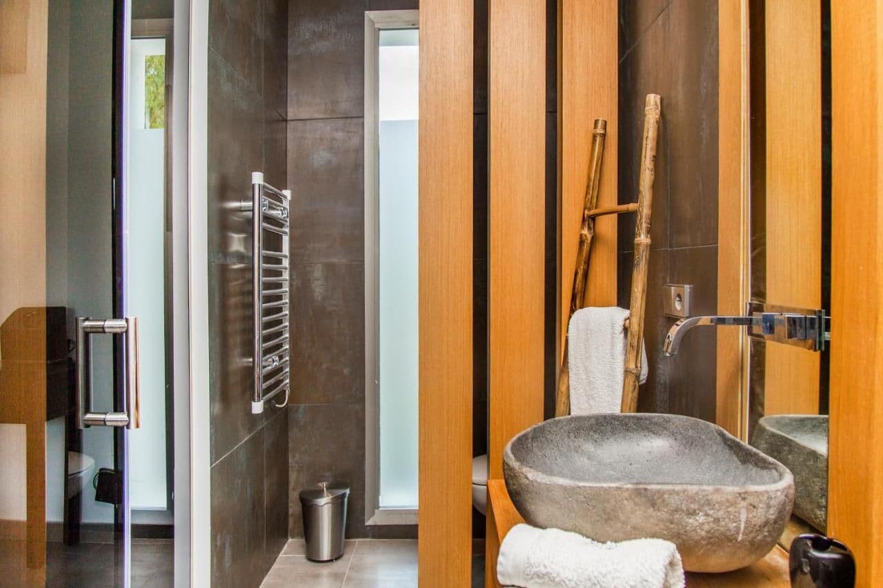 Dark tiled bathroom with a stone trough sink and ladder shelving