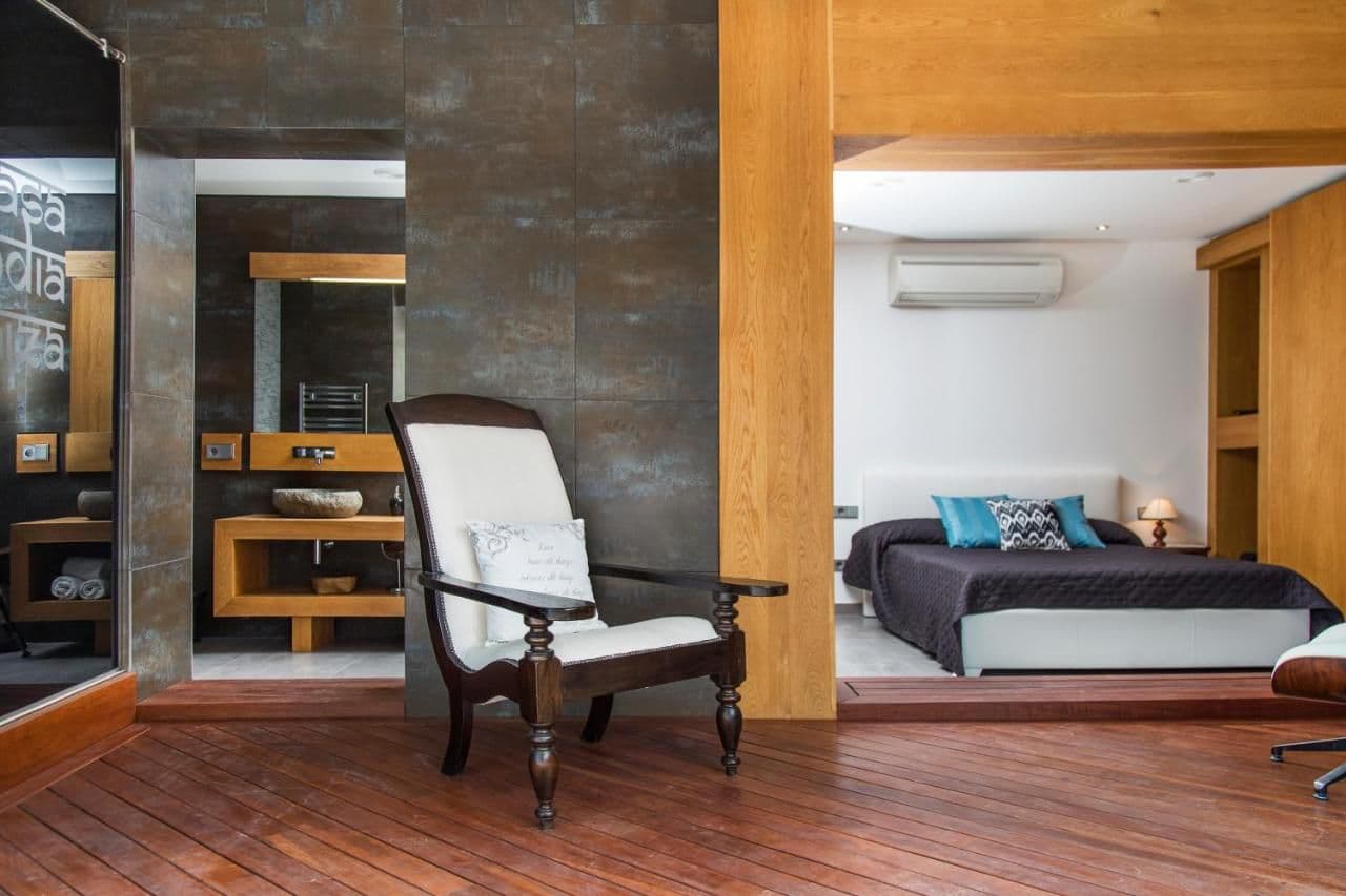 Bedroom with dark wood beams, a white armchair and wood flooring