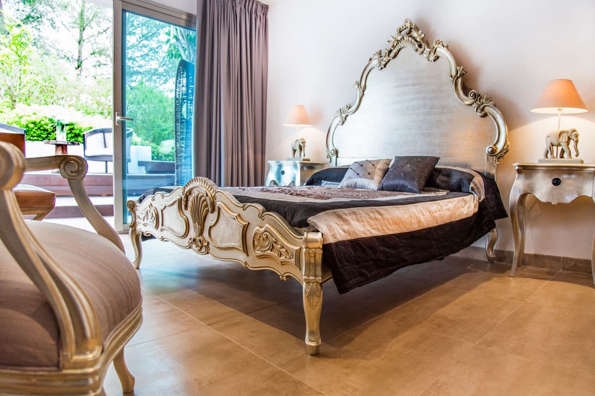 Bedroom with an ornate gilded mirror headboard and garden views