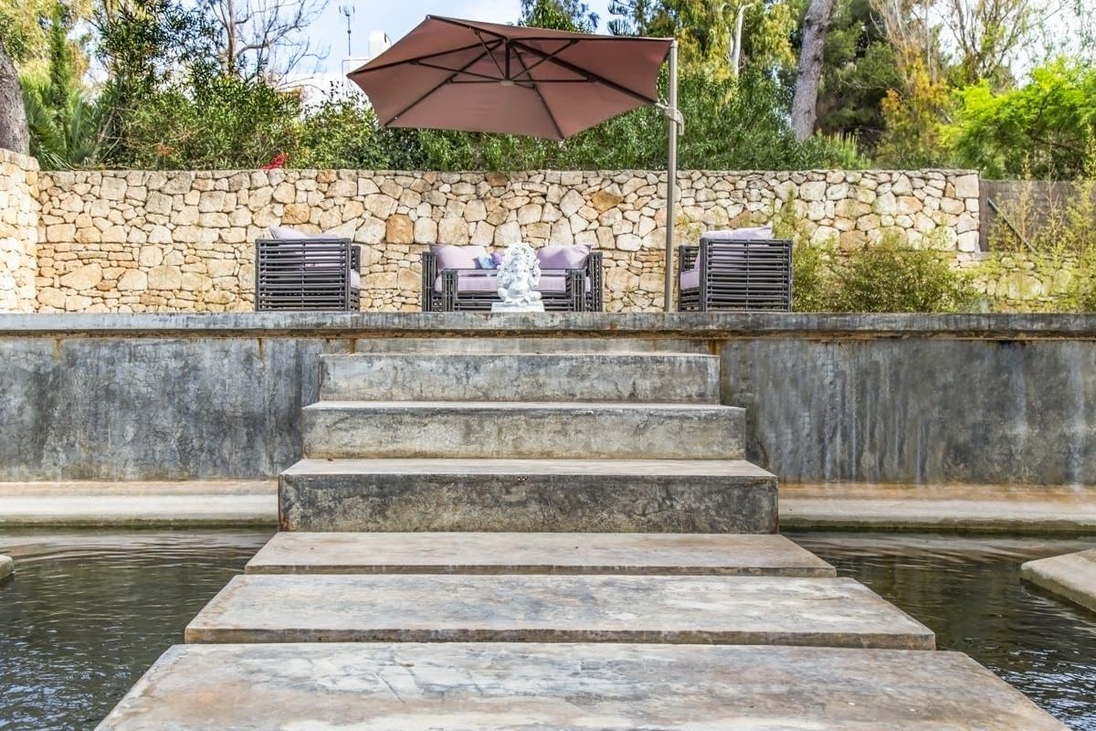 Stone stepping stones crossing a reflecting pond towards lounge seating