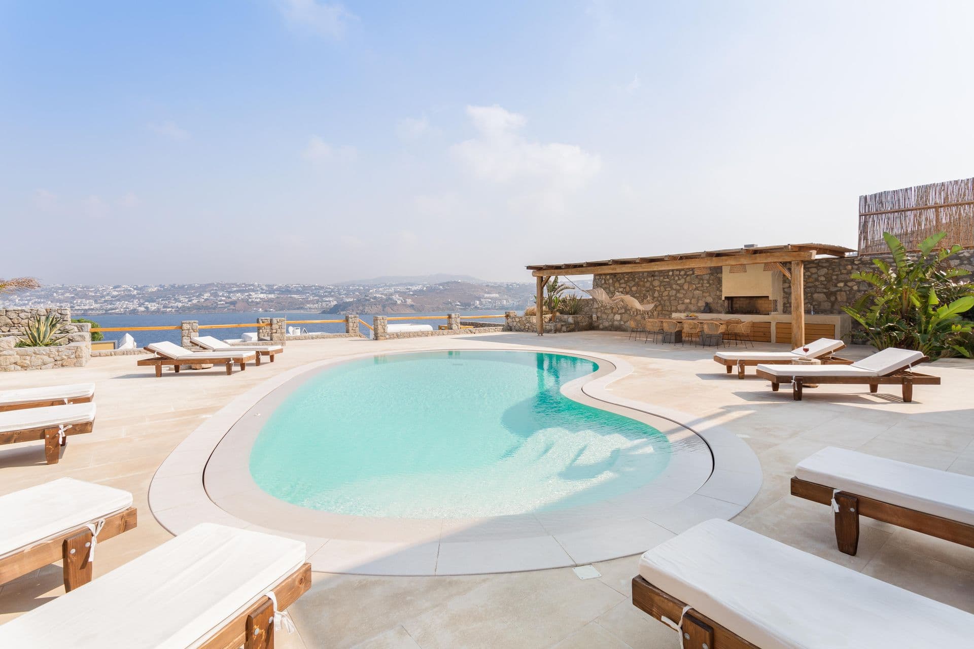 Curved pool with wooden sun loungers set against a clear blue sky