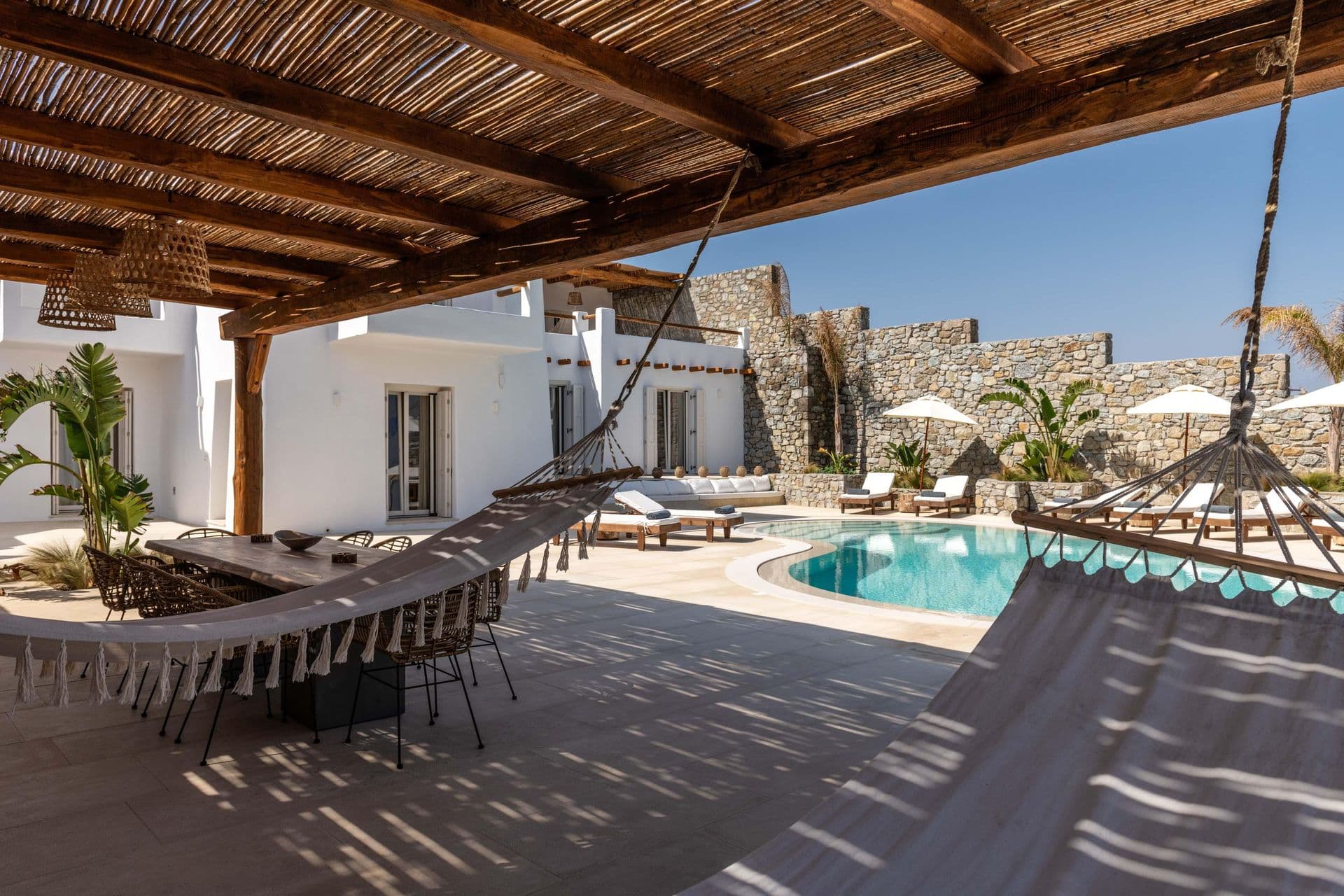 Outdoor terrace with long dining table, pool and stone boundary wall