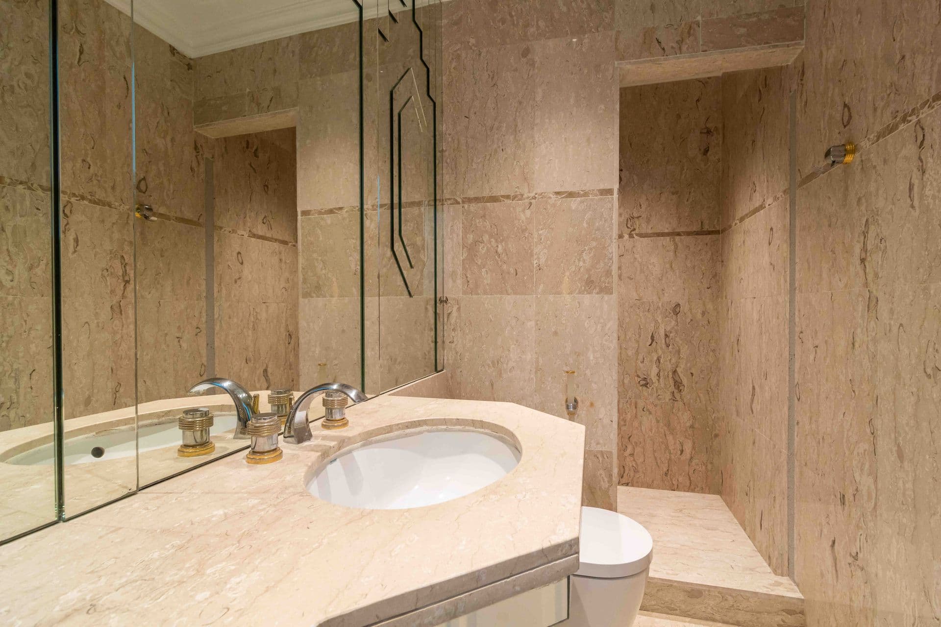 A travertine bathroom with a marble vanity and mirrored walk in shower