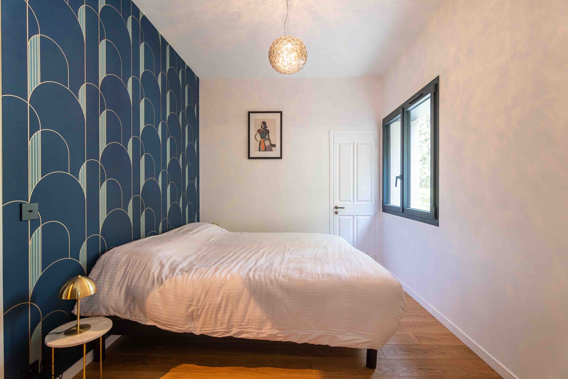 A bedroom with bold scalloped wallpaper and a brass pendant light
