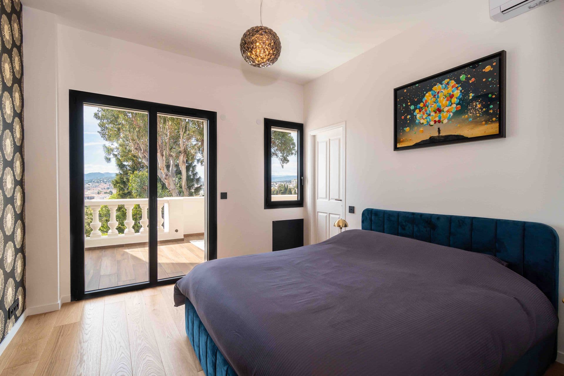 A bedroom with a teal upholstered bed and glazed doors onto a private terrace