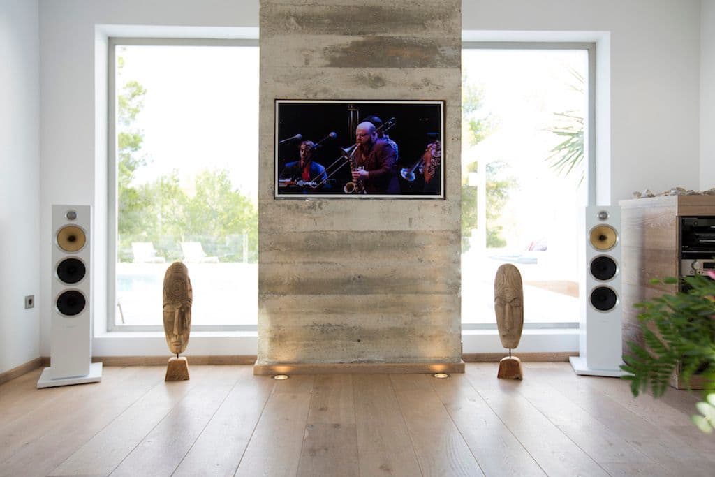 Lounge with a television on a board-formed concrete wall and floor speakers at Between Pines, Ibiza