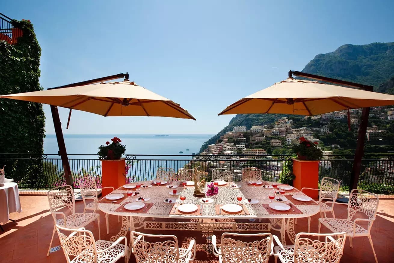 Long dining table set under umbrellas with a coastal backdrop