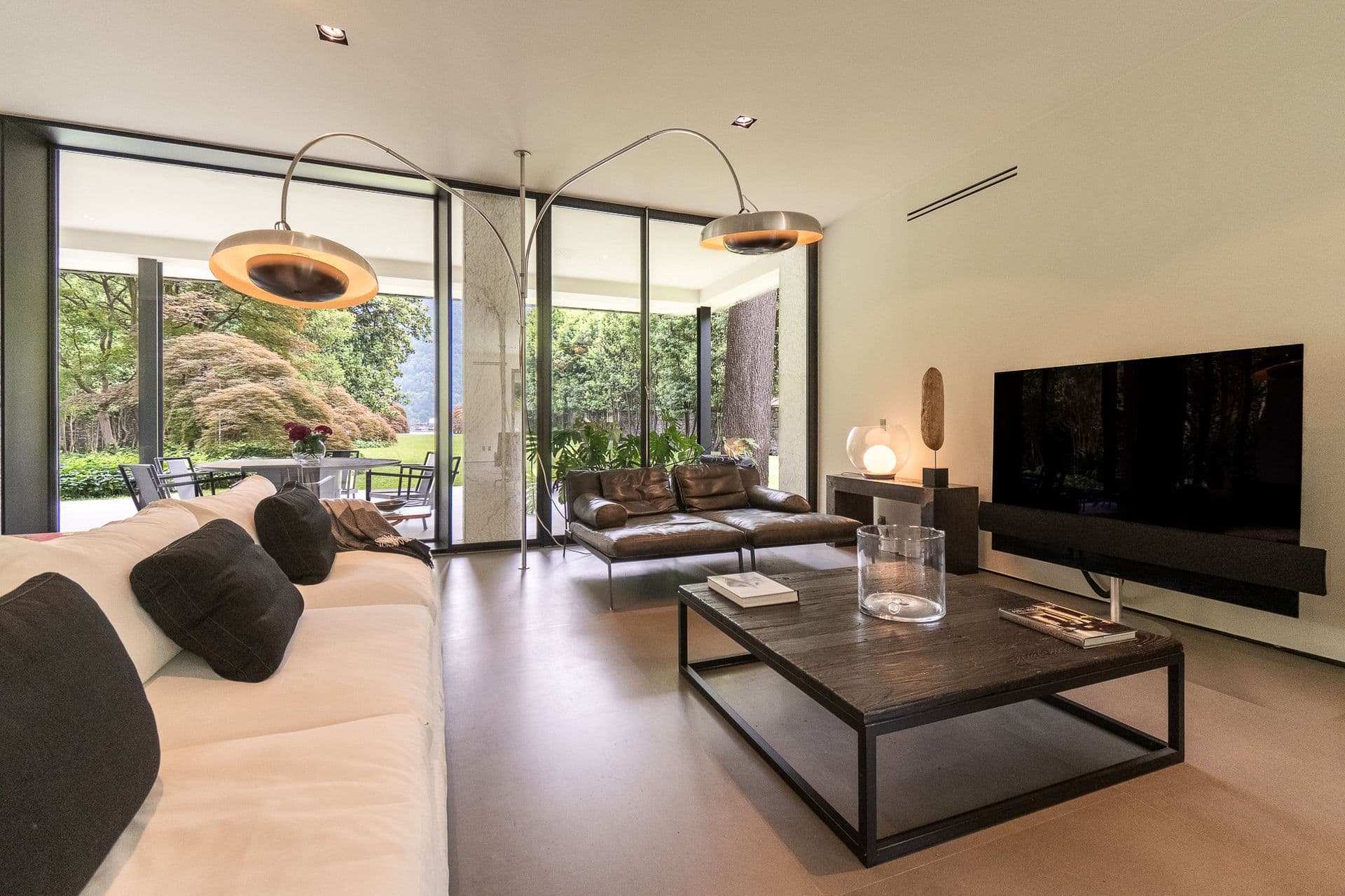 Lounge with a black sofa and television against a glass wall to the garden at Elegant Lake Manor, Cernobbio