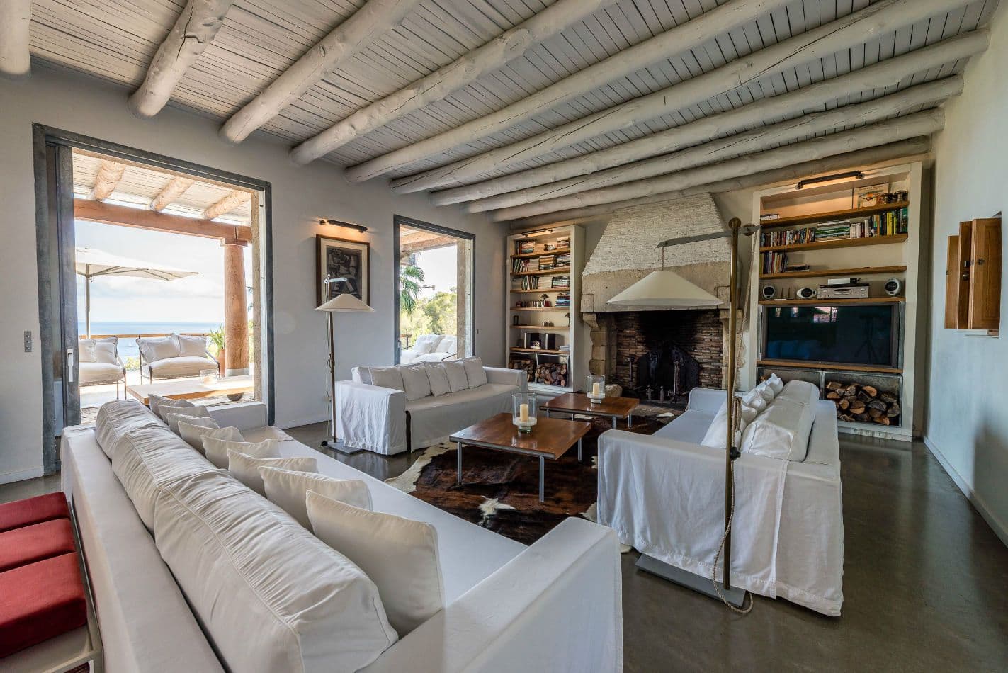 Long living room with white slipcovered sofas and an open fireplace