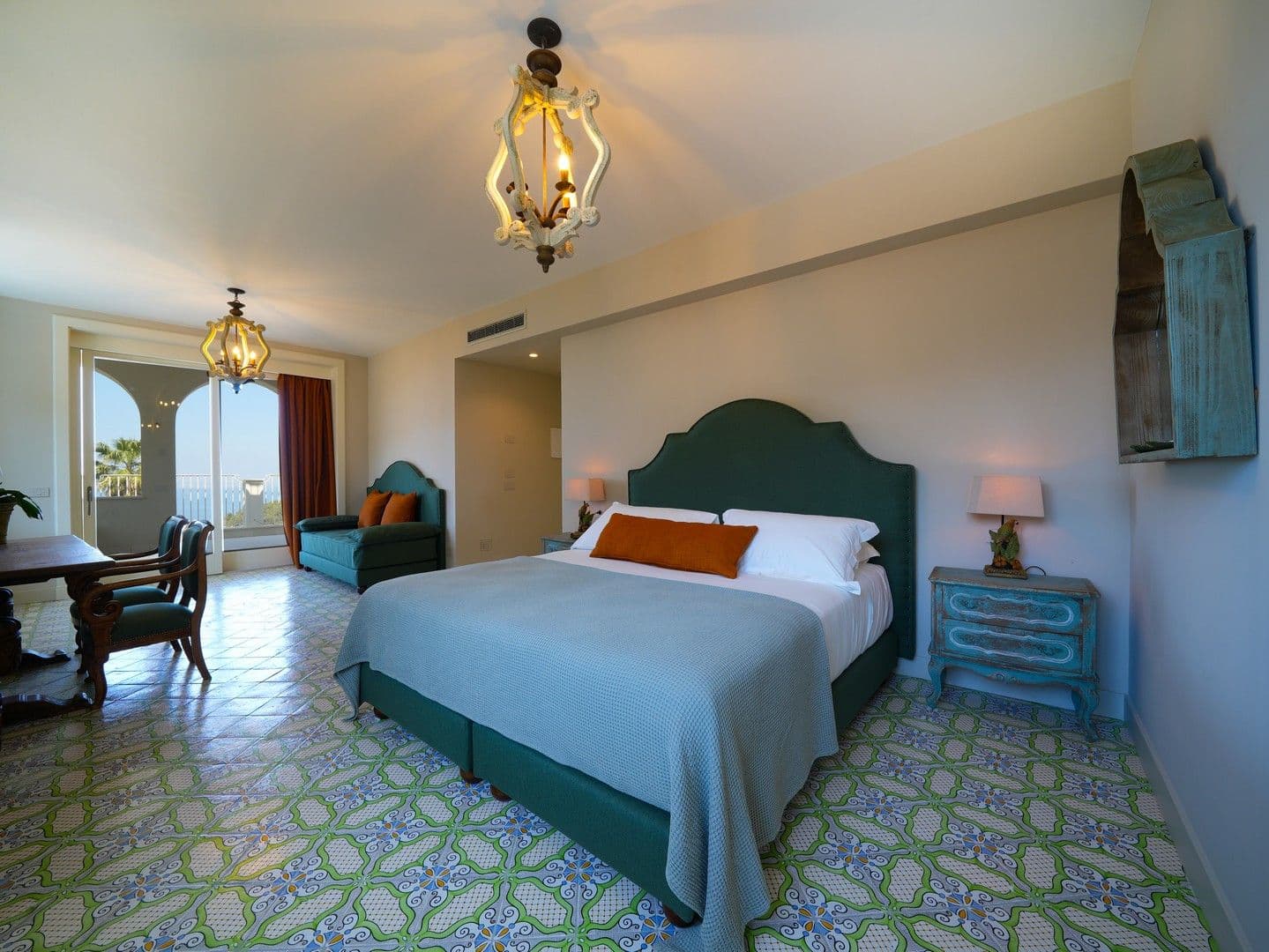 Master bedroom with a teal headboard and majolica-tiled floor opening to the sea at Casarlano Sunsets, Sorrento