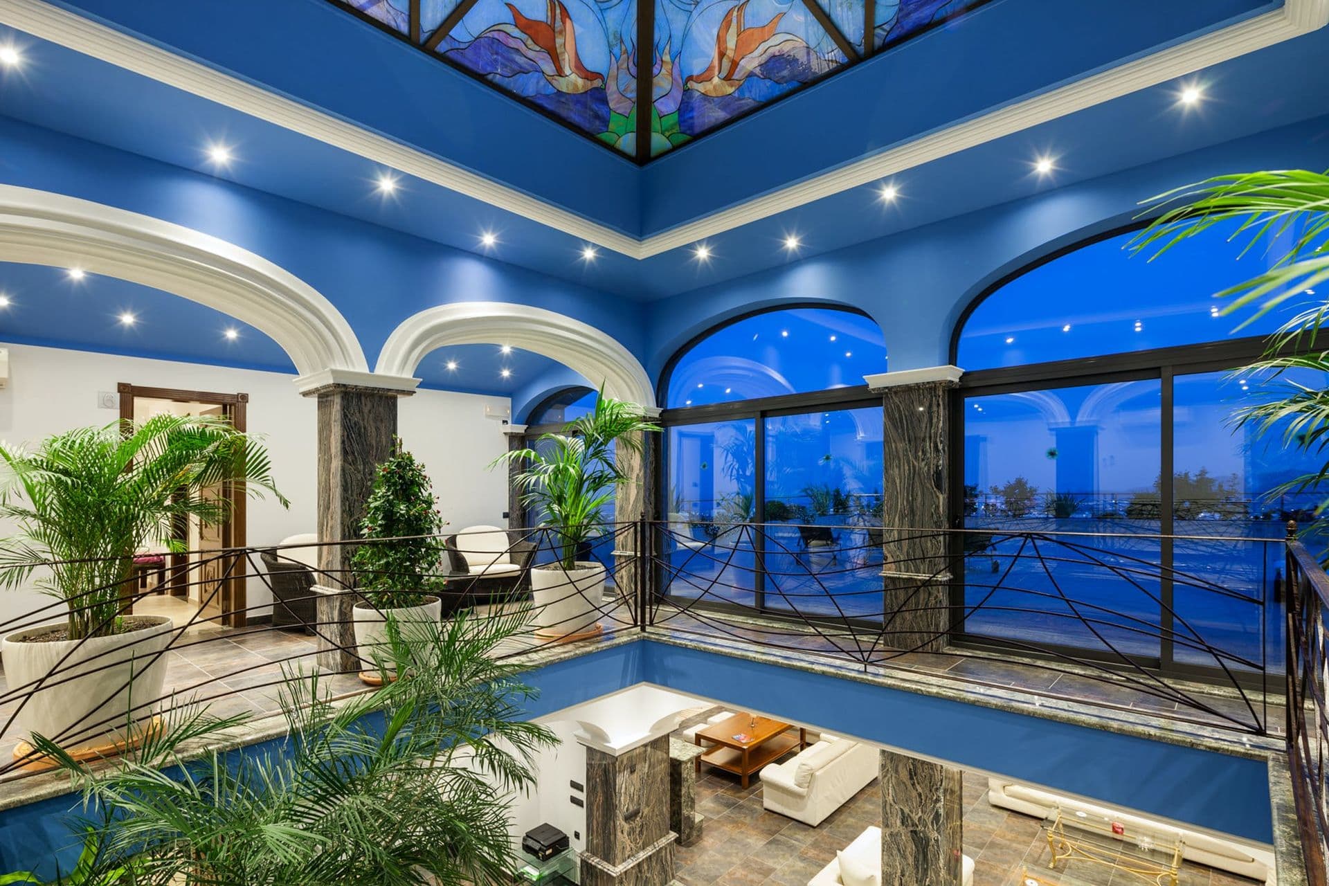 Dramatic indoor atrium with stained-glass ceiling and columned arches lit blue at dusk