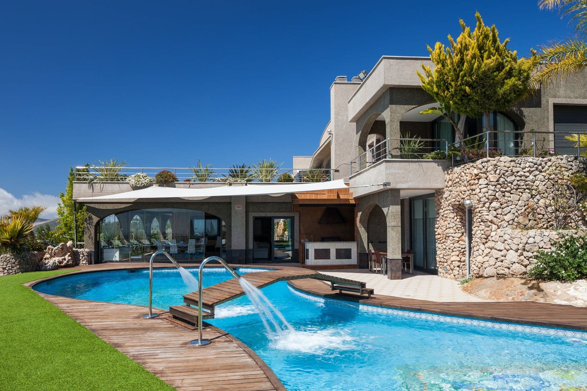 Ibizan villa with a curved pool, waterfall feature and terraced garden under a clear sky