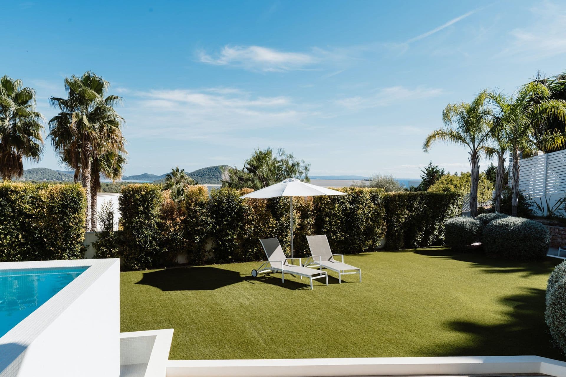 Pool corner bordered by lawn and sun loungers under palm trees at Hazy Island View
