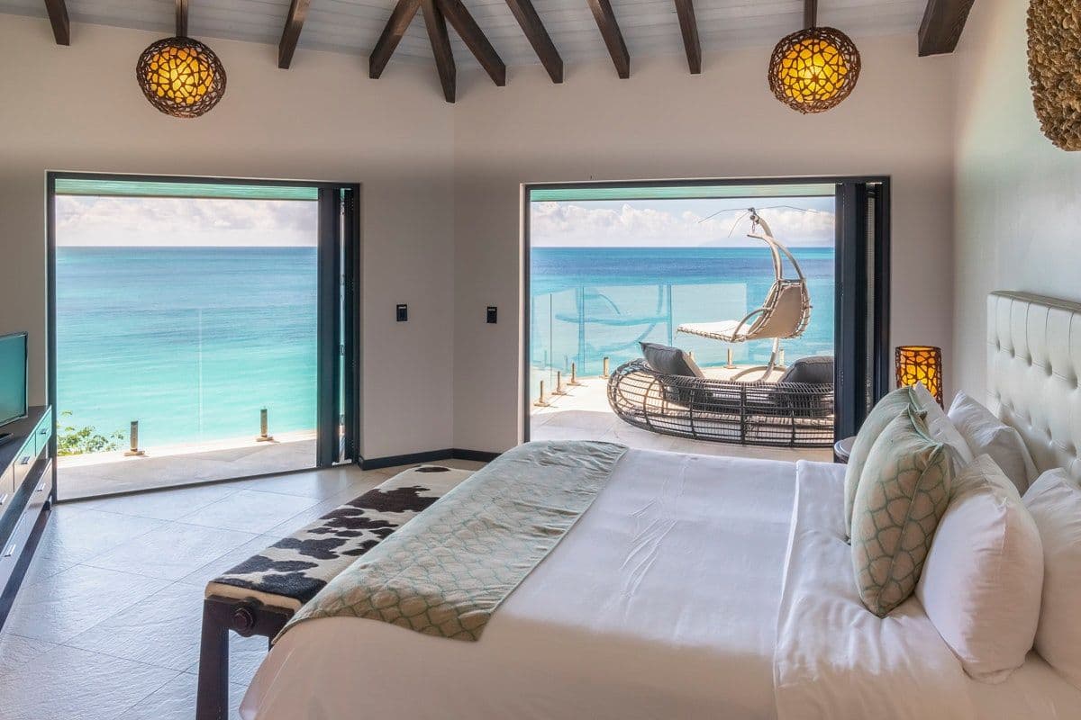 Master bedroom opening to a sea-view balcony with a hanging chair at Views in the Tropics