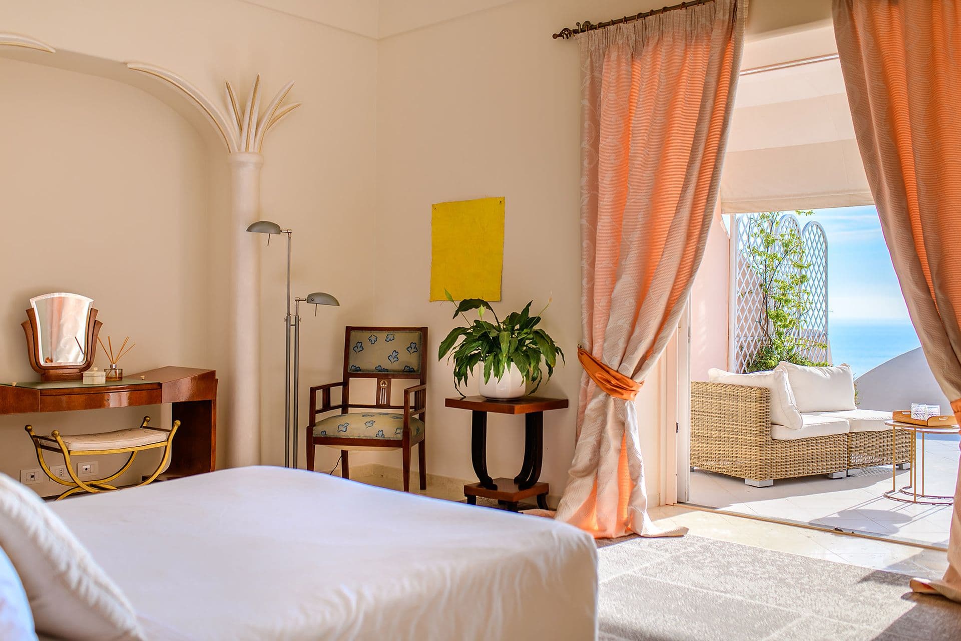 Bedroom corner with an armchair and artwork beside tall windows