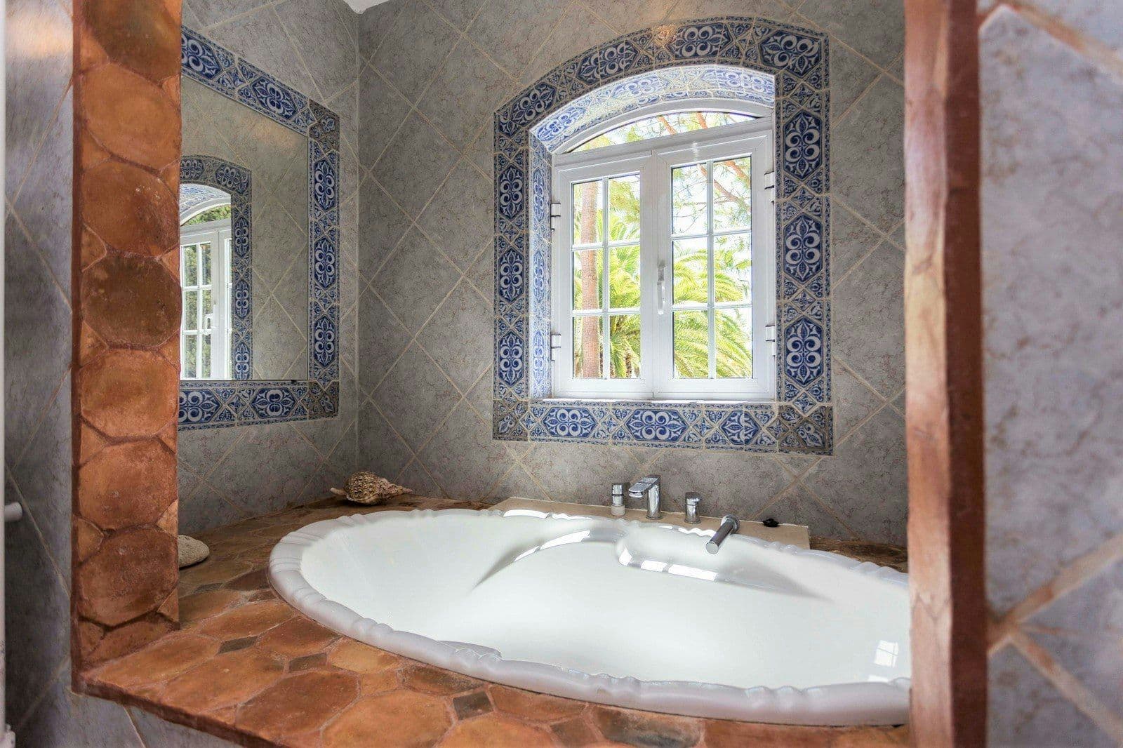Tiled bathroom with a corner bath and painted azulejos at Your Algarve Oasis