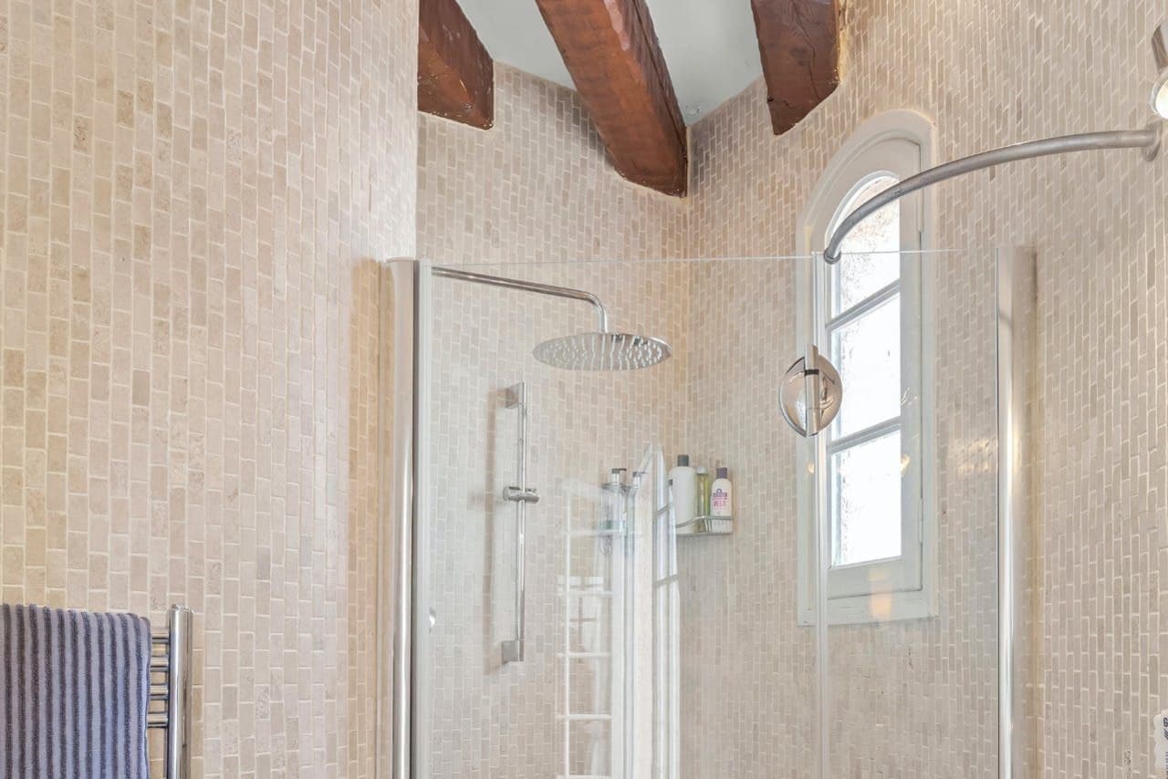 Ensuite bathroom with rainfall shower and mosaic-tiled walls beneath exposed beams
