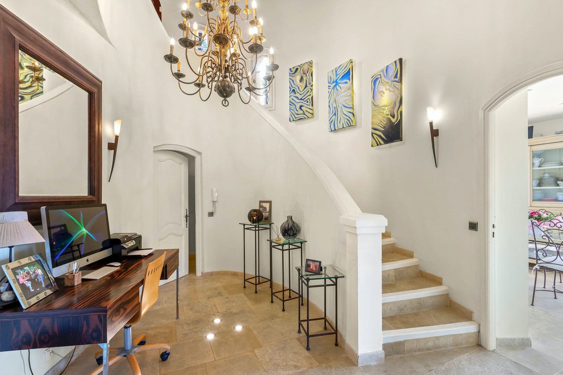 Entrance hall with study desk and curved staircase beneath a wrought-iron chandelier