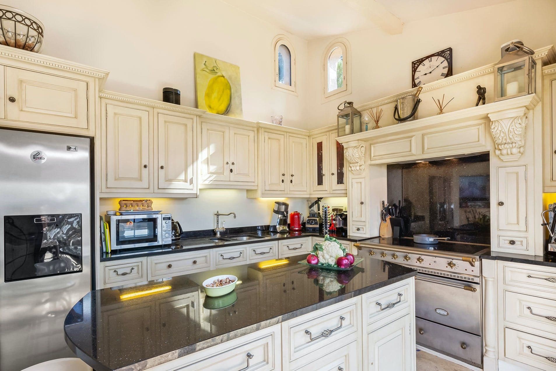 Kitchen island with black granite worktop, integrated appliances and cream cabinetry