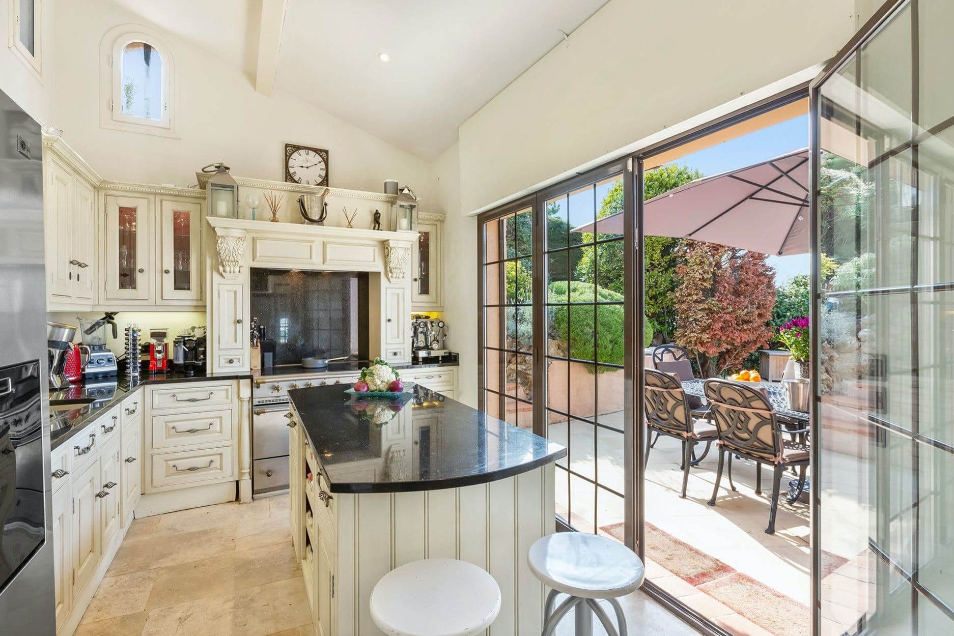 Cream farmhouse-style kitchen with fireplace and doors opening onto the outdoor dining terrace