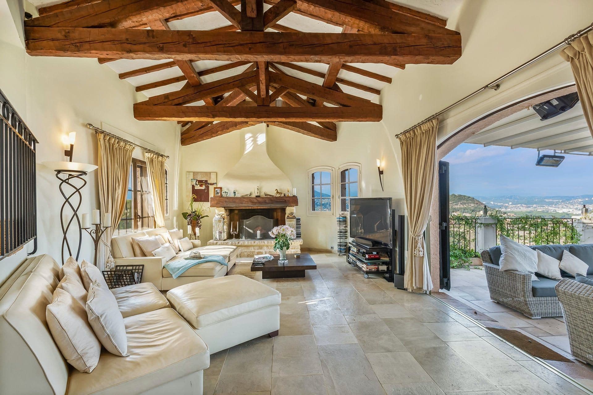Open-plan living room with exposed wooden beams, fireplace and folding doors leading to the terrace