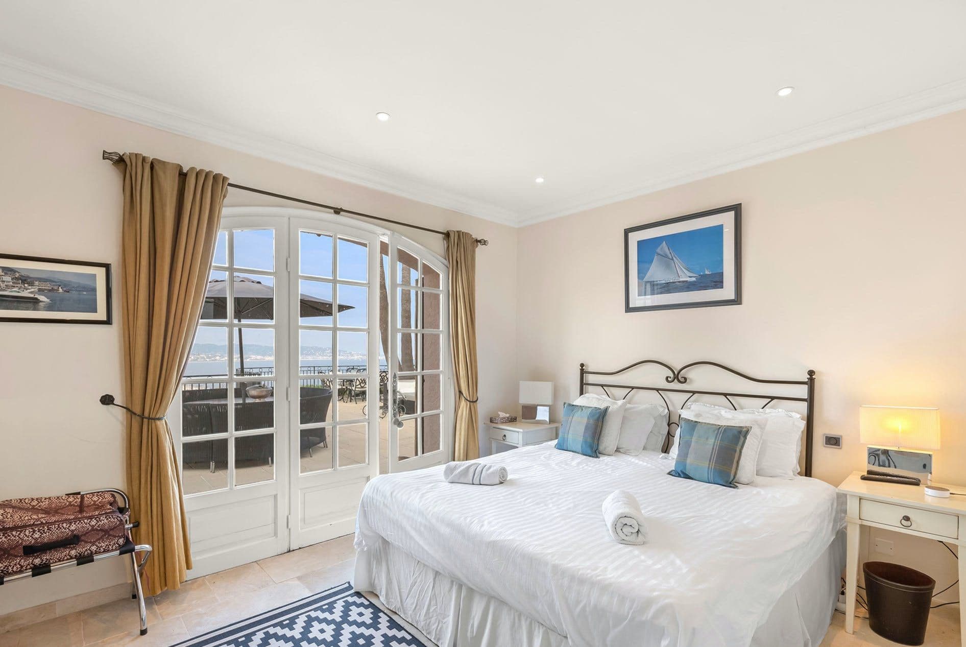 Bedroom with wrought-iron bed frame, striped bedding and French doors opening onto a sea-view balcony