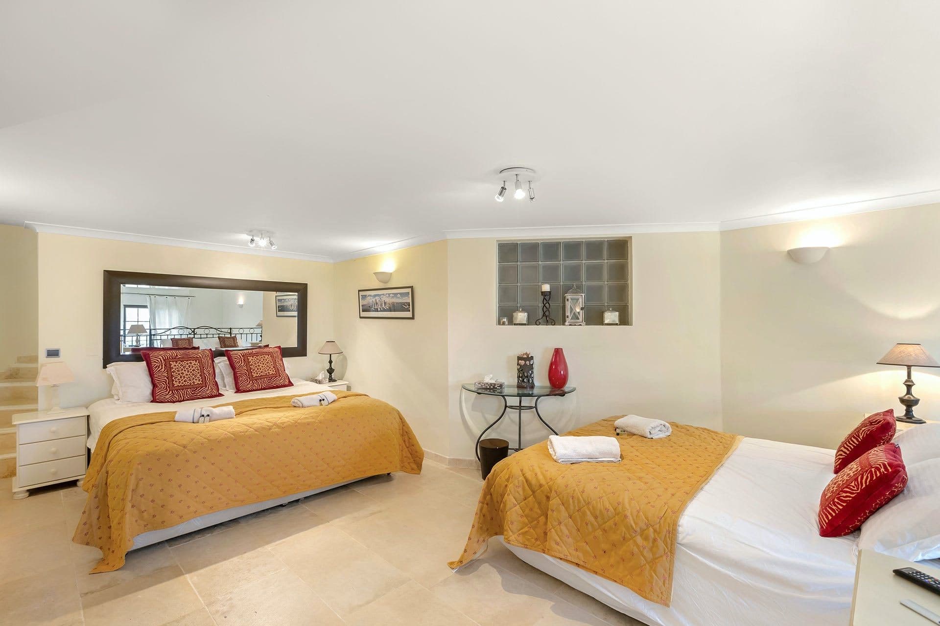 Twin bedroom with mustard and red accent cushions and garden-facing windows