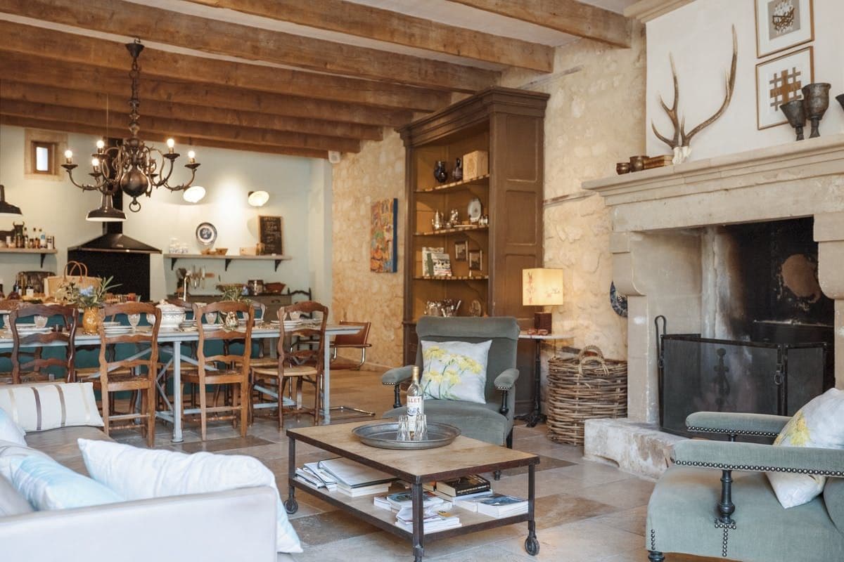Long farmhouse dining table beneath exposed beams and fireplace