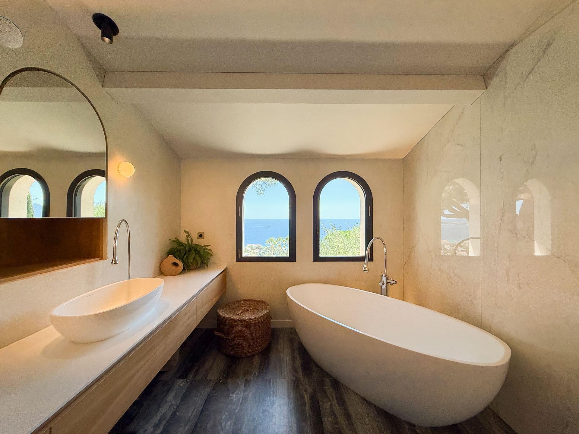 Marble bathroom with a freestanding tub and twin basins below arched sea-view windows at An Azure Vision, Cannes