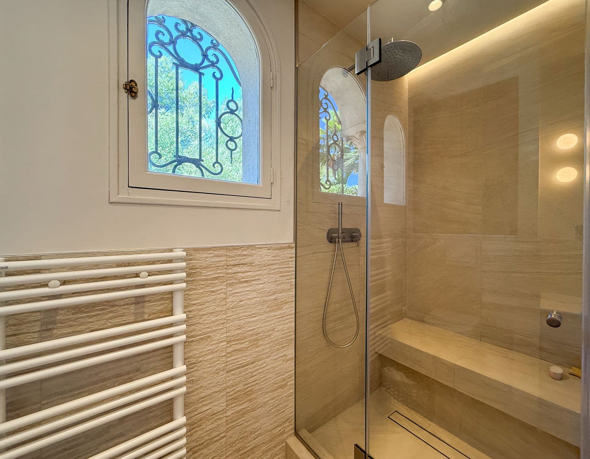 Walk-in stone shower lit by a stained-glass arched window at An Azure Vision, Cannes
