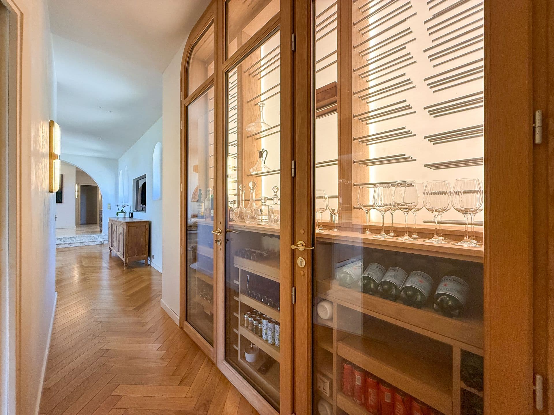 Glazed wine and glassware cabinet in a parquet hallway at An Azure Vision, Cannes