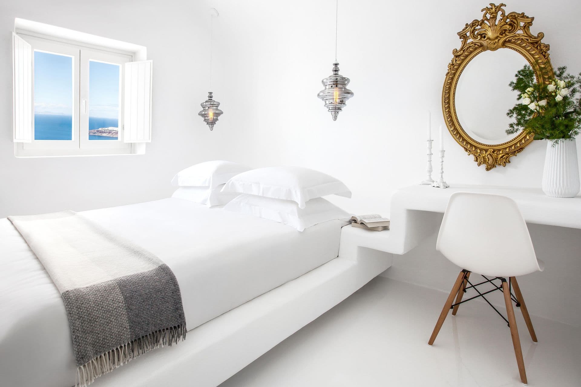 White cave bedroom with a sea-view window and a gilt mirror at Cave Chic, Imerovigli, Santorini