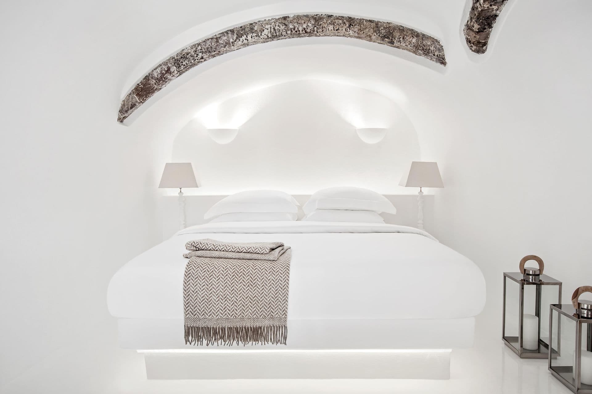 White cave bedroom with glass lanterns and a grey throw at Cave Chic, Imerovigli, Santorini
