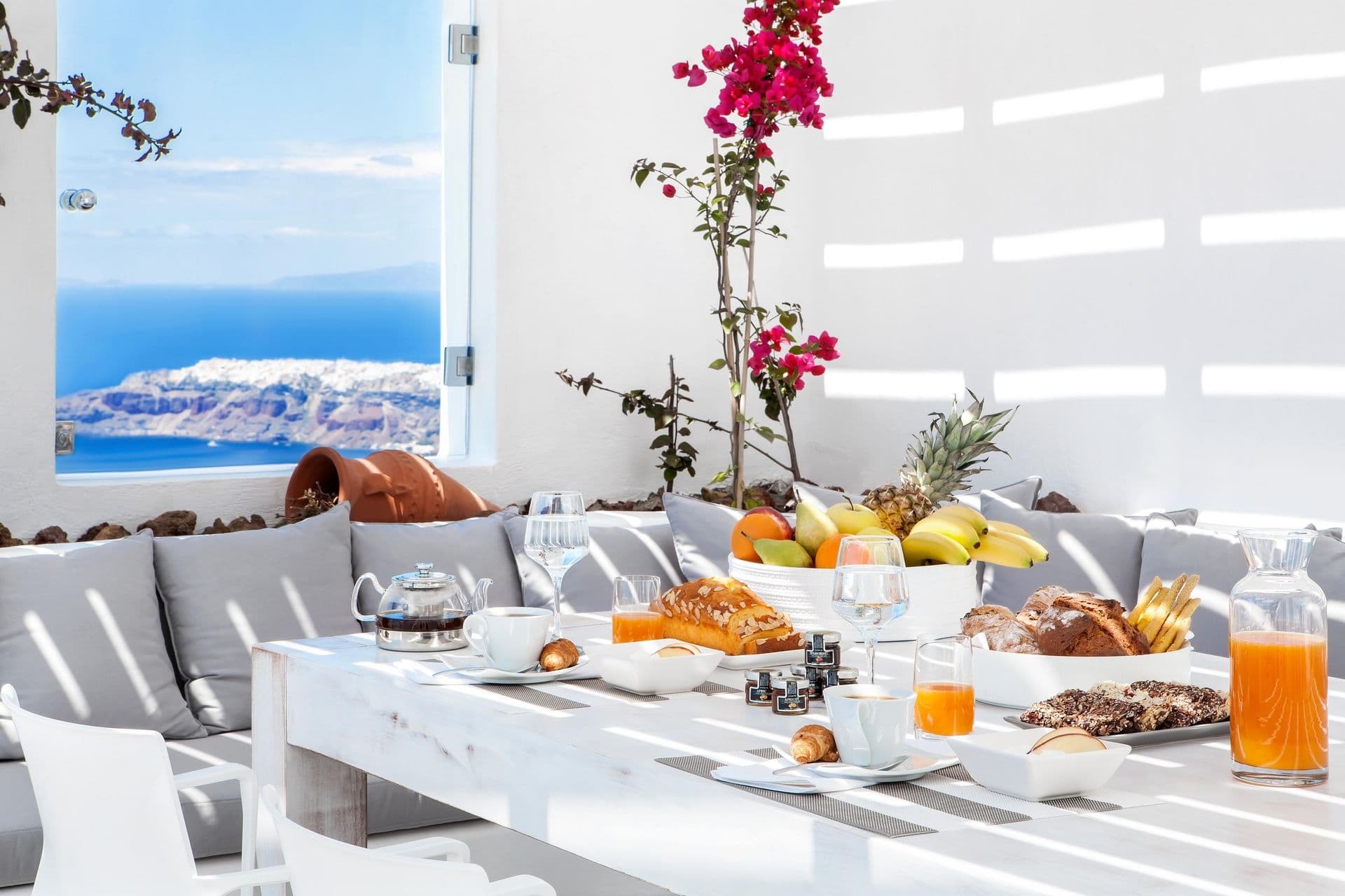 Breakfast laid on a terrace table with bougainvillea and a caldera view at Cave Chic, Imerovigli, Santorini