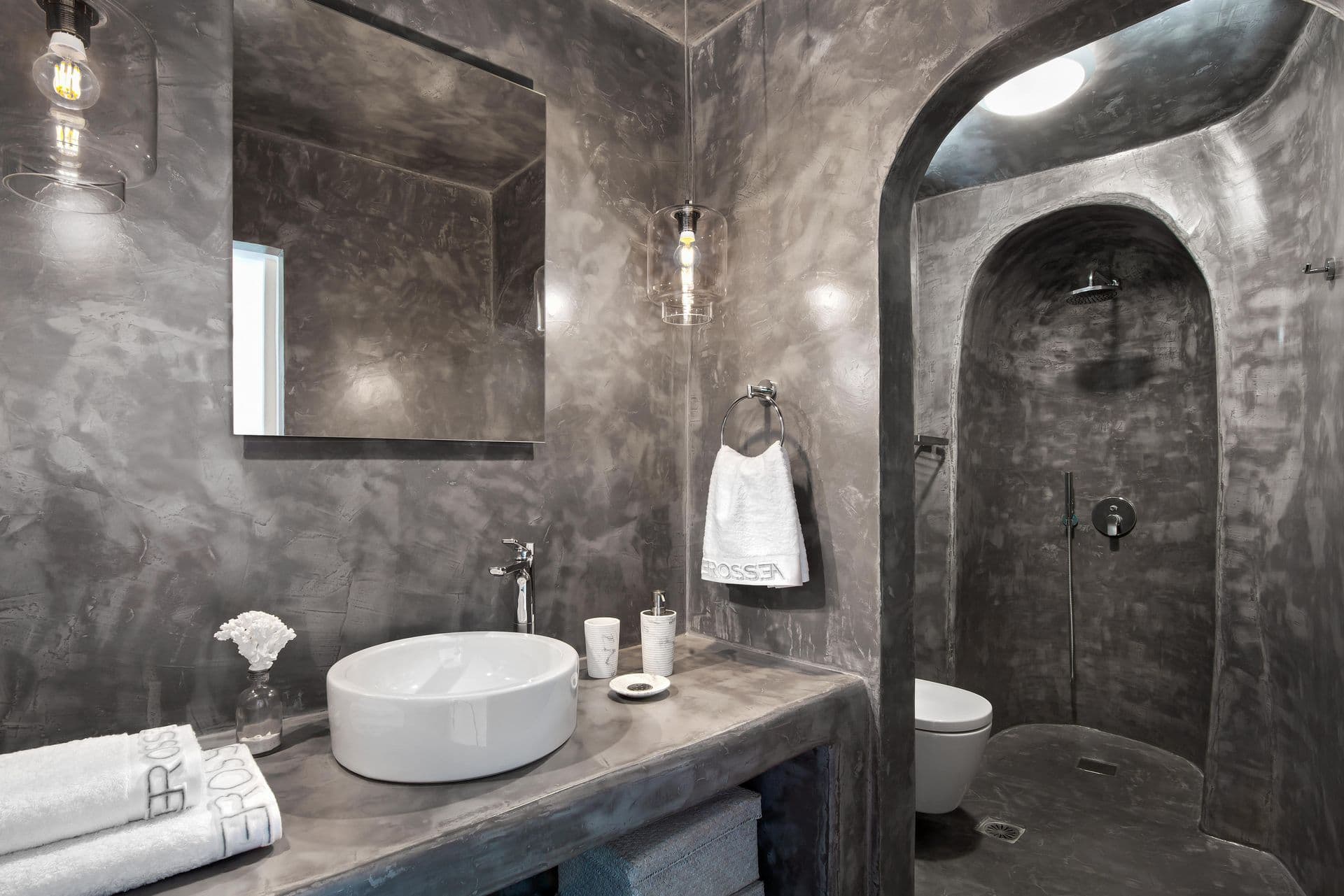 Grey microcement cave bathroom with a curved walk-in shower at Cave Chic, Imerovigli, Santorini