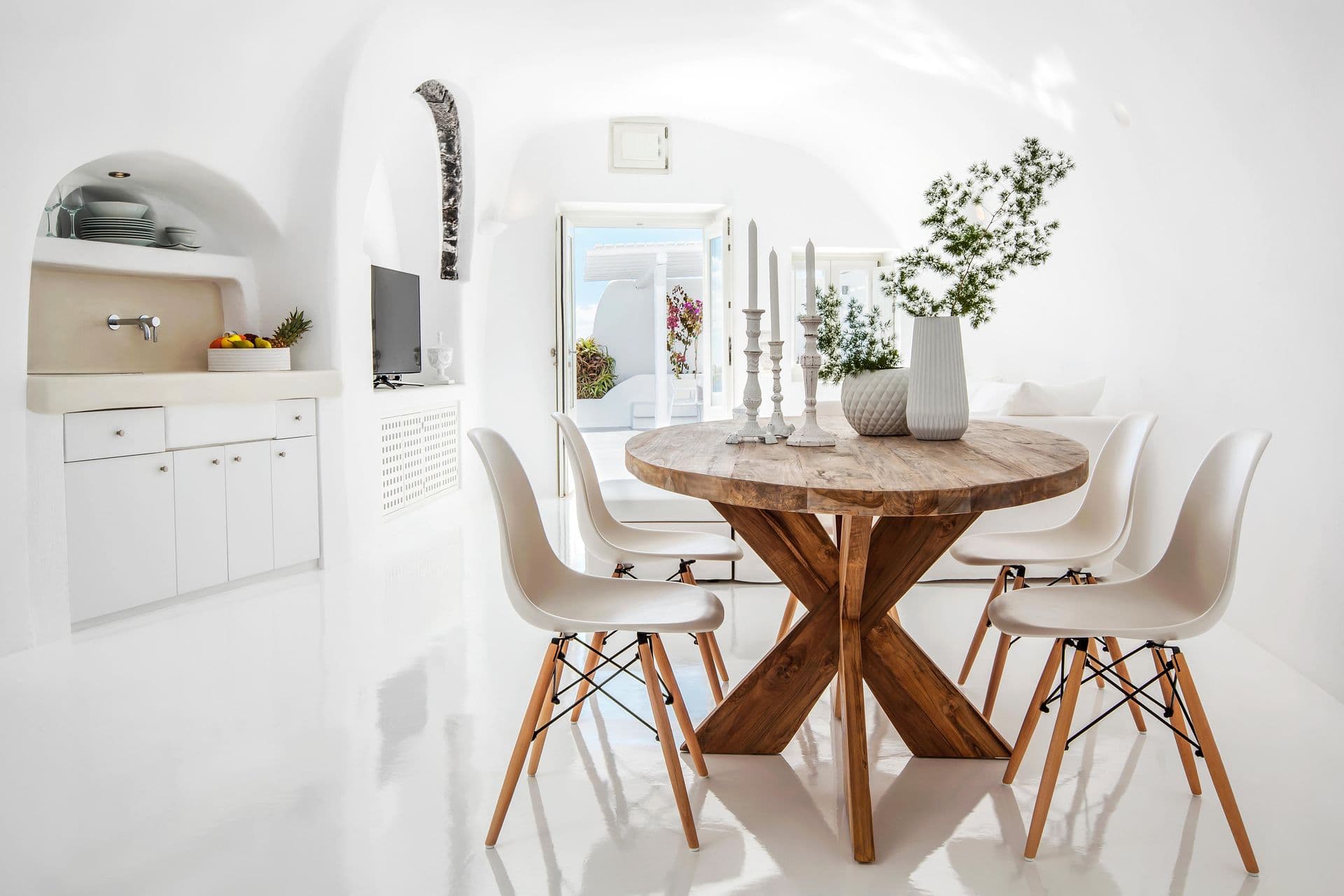 White cave dining room with a round timber table and Eames chairs at Cave Chic, Imerovigli, Santorini