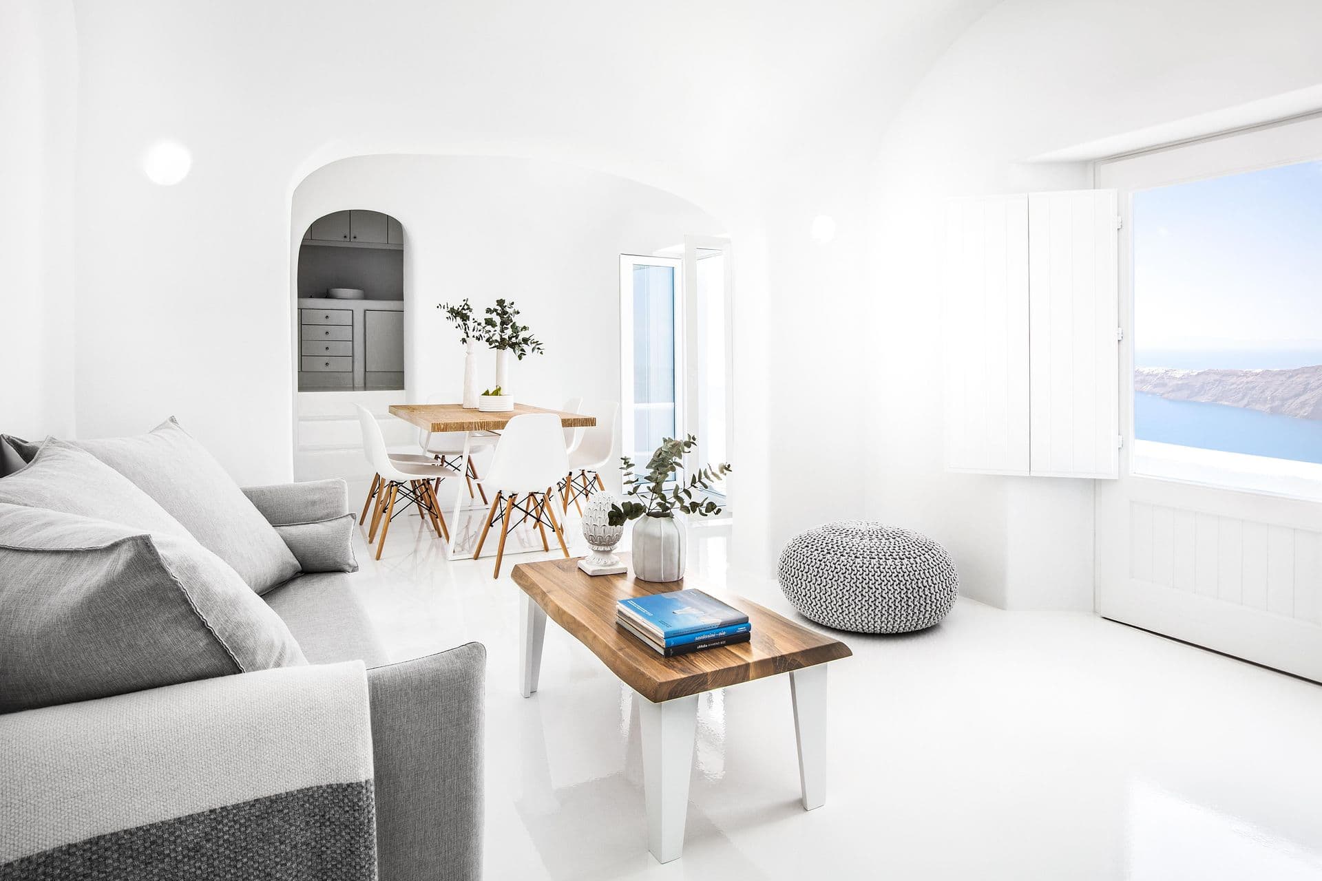 White cave living room with grey sofas and a caldera-view window at Cave Chic, Imerovigli, Santorini