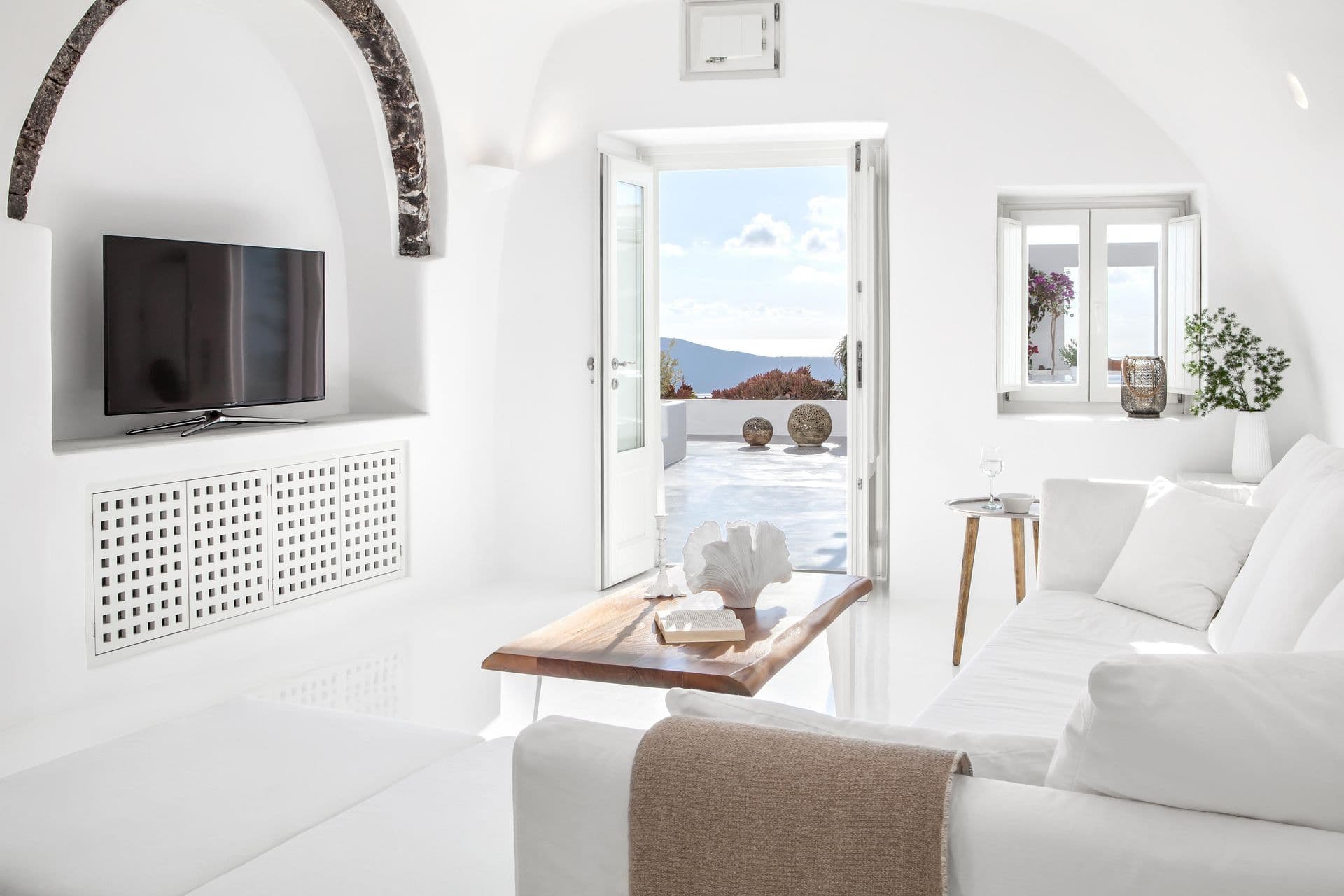 White cave lounge with a television opening to the terrace at Cave Chic, Imerovigli, Santorini