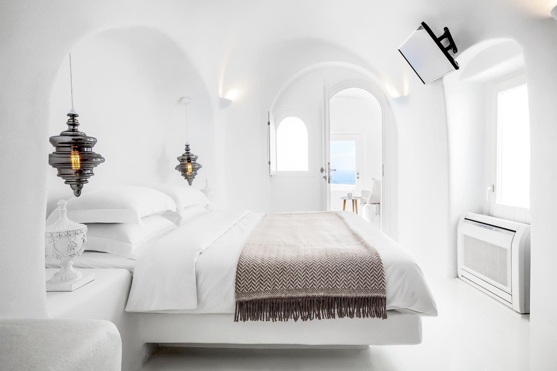 White cave bedroom with black pendant lights and an arched sea view at Cave Chic, Imerovigli, Santorini