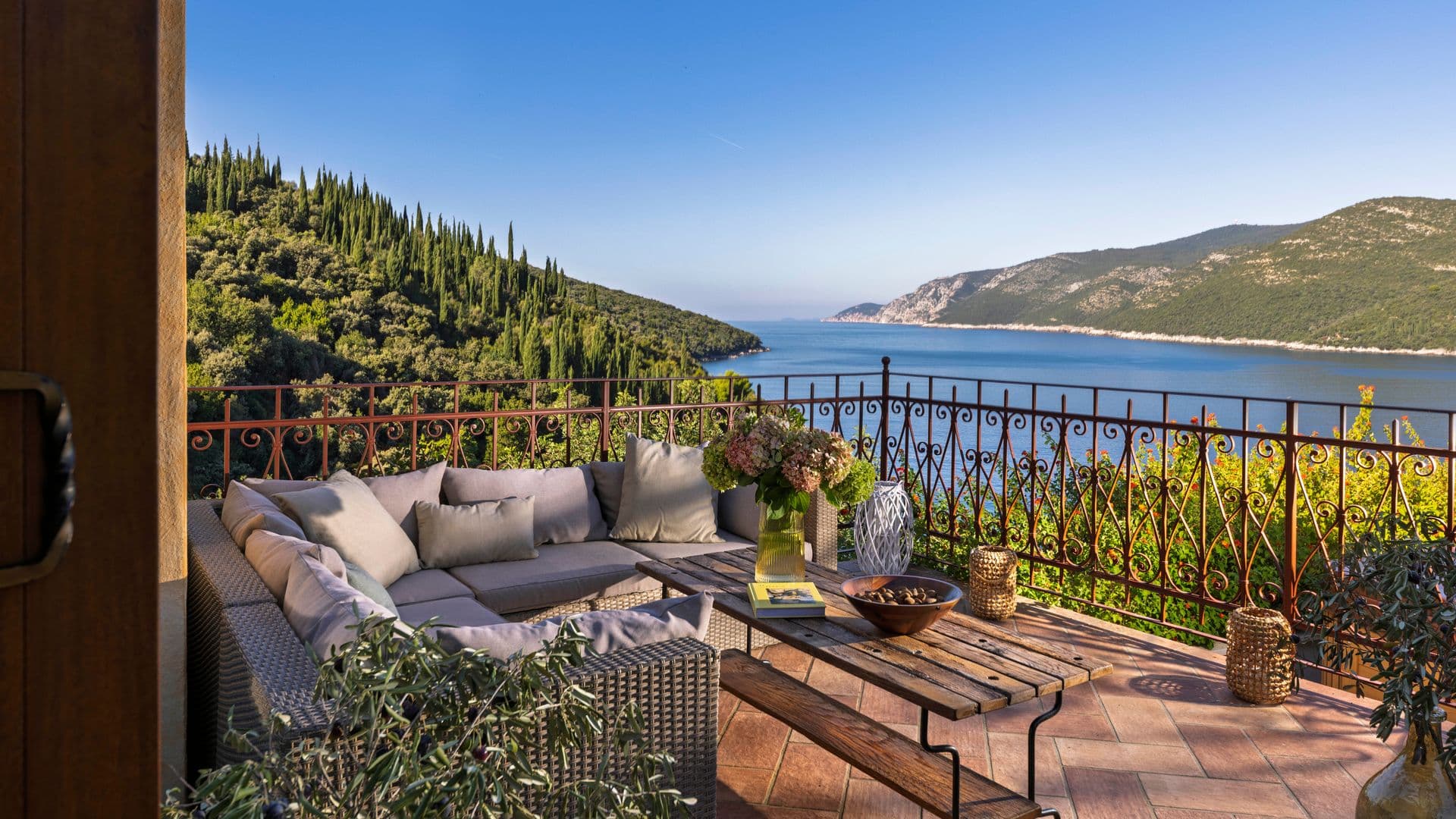 Terrace lounge with a corner sofa and wrought-iron railing above the bay at Aria to the Adriatic, Croatia