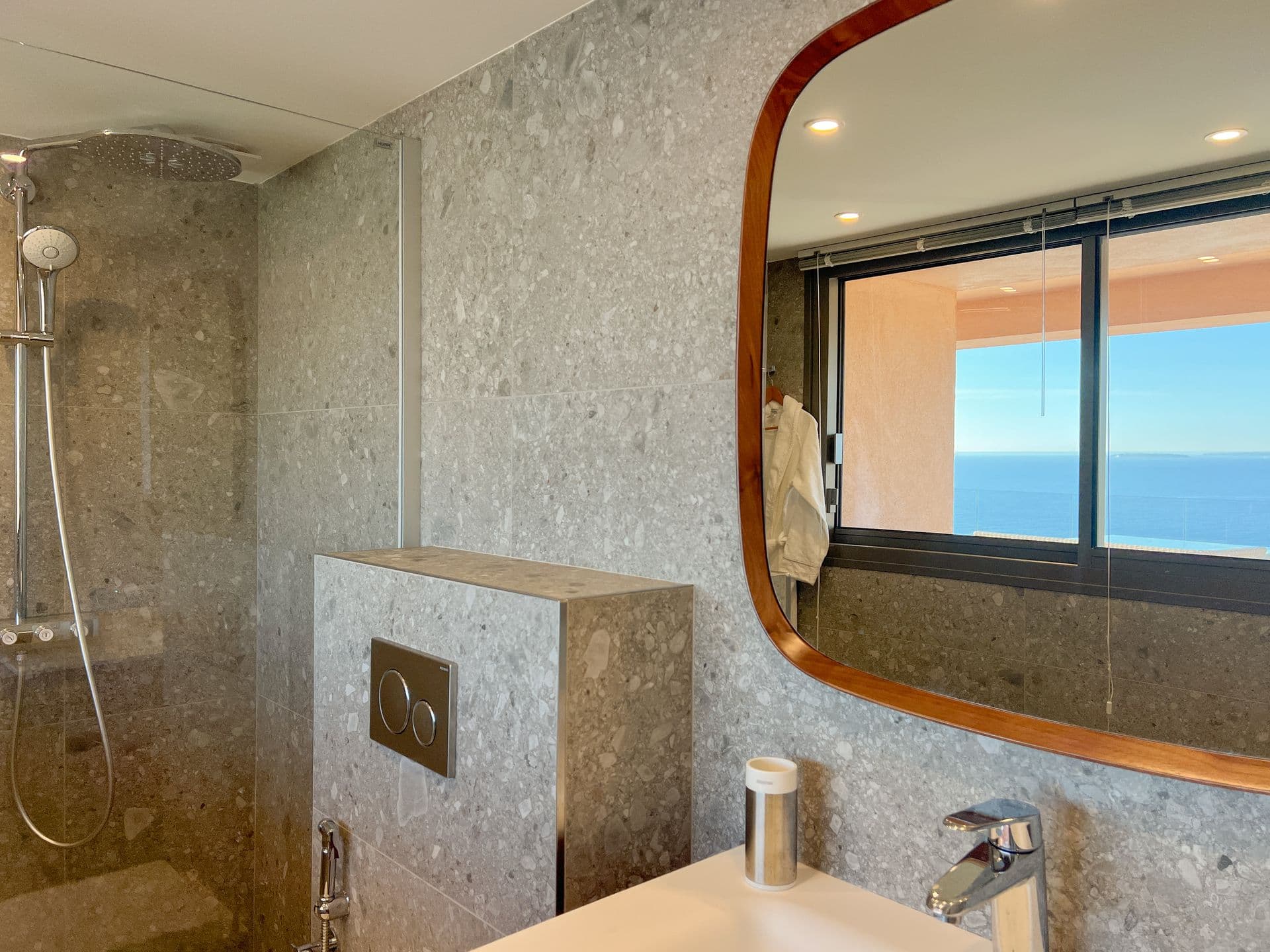 Marble-tiled shower room with a curved mirror and coastal-facing window
