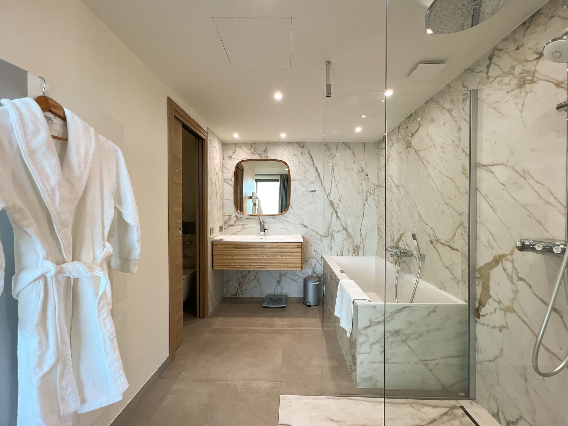 Bathroom with a bathrobe hung beside a glass-walled shower and stone floor